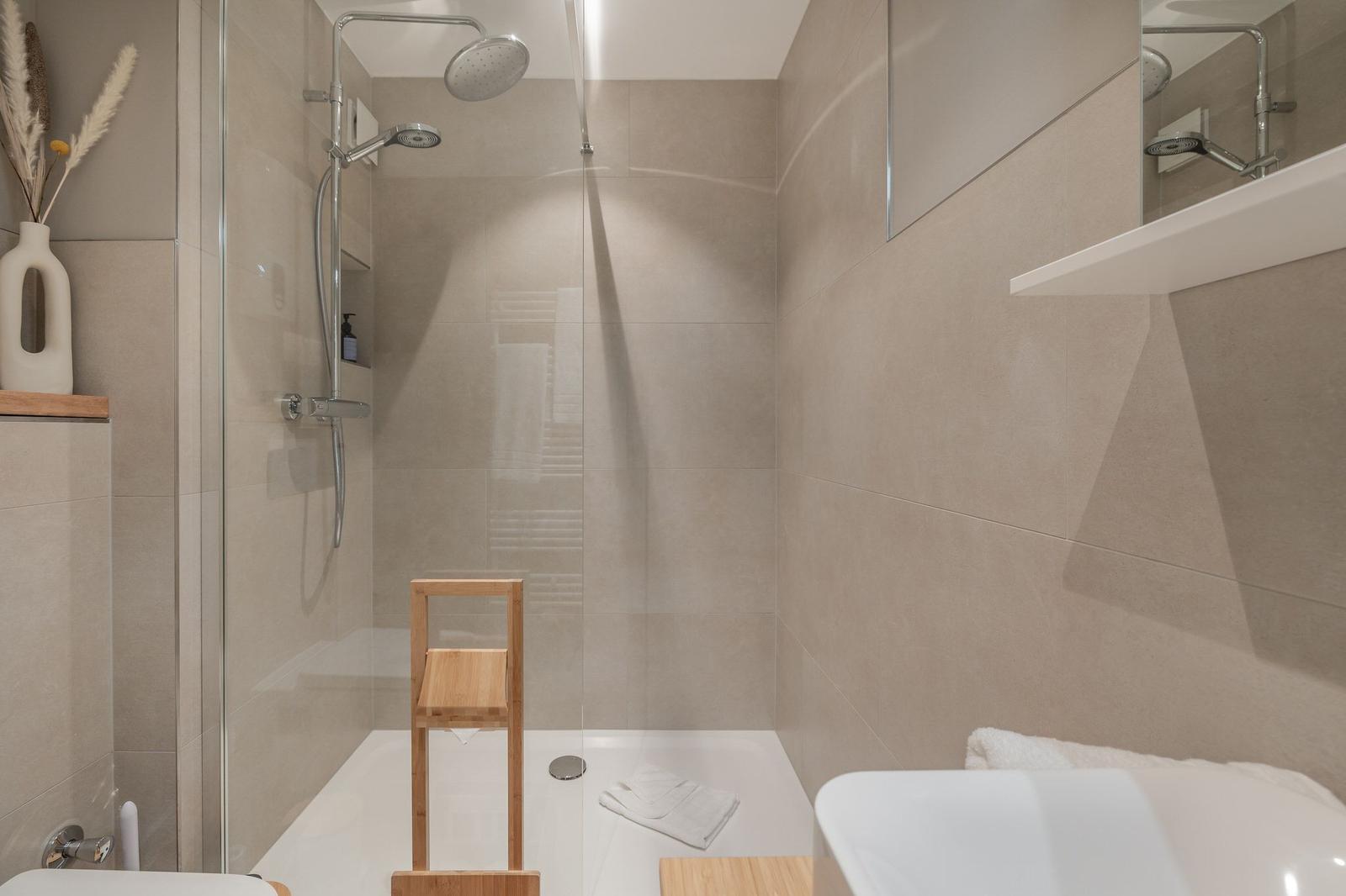 Dusche mit Glaswand, Holzstuhl und Waschbecken