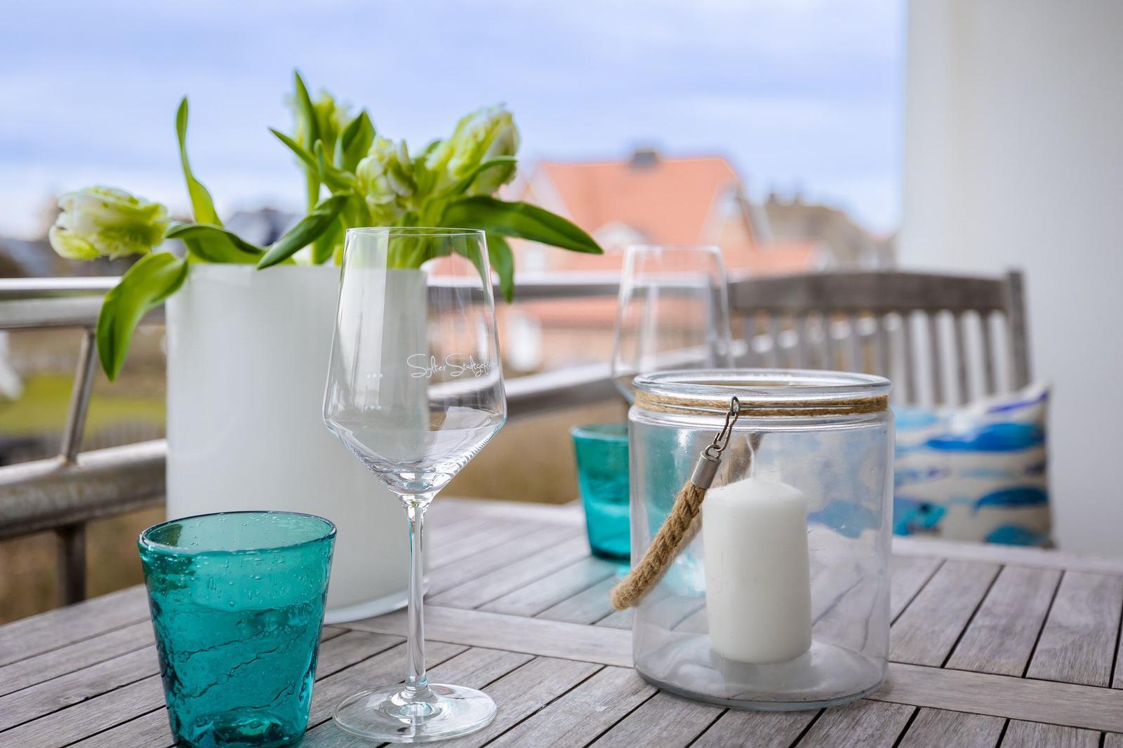 Terrasse mit Tisch, Gläsern, Kerze und Blumen. Hintergrund: Dachhäuser.