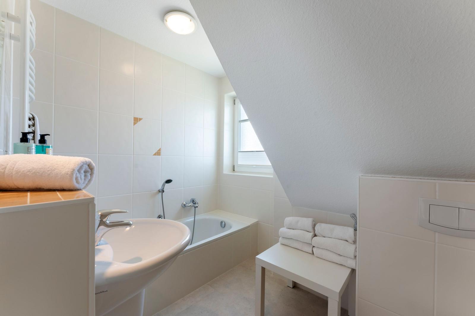 Badezimmer mit Badewanne, Waschbecken und Fenster unter Dachschrägen.