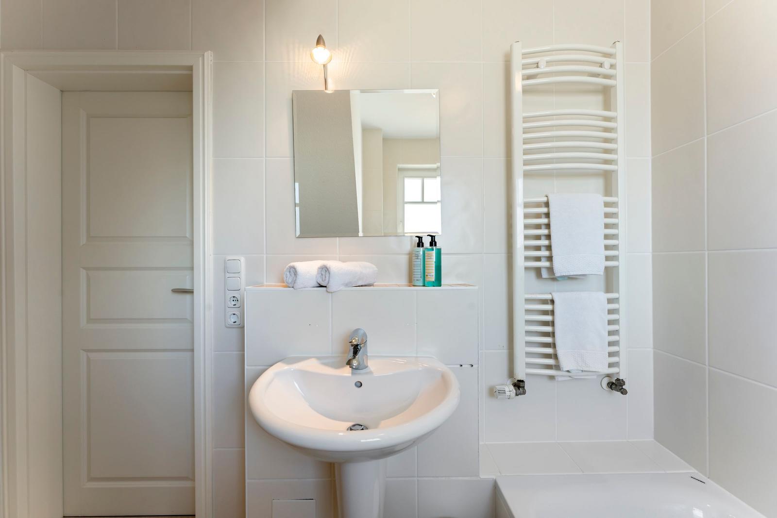 Badezimmer mit Waschbecken, Spiegel, Handtüchern und Heizkörper