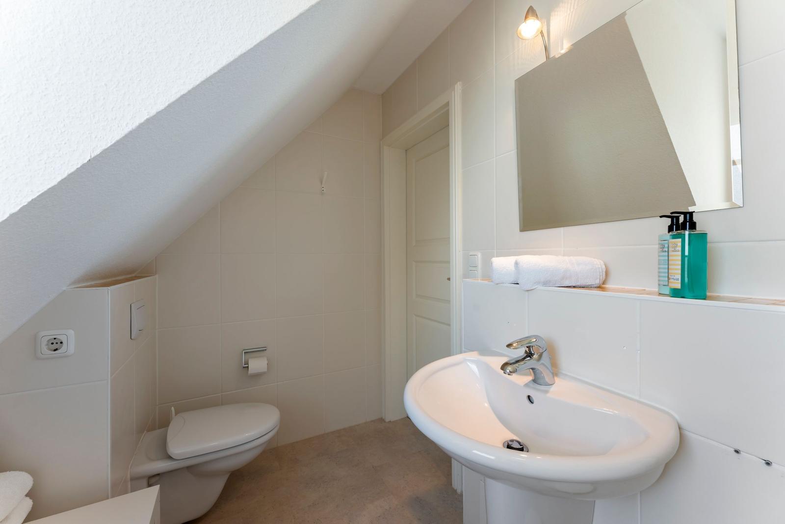 Badezimmer mit Toilette, Waschbecken und Spiegel unter Dachschräge