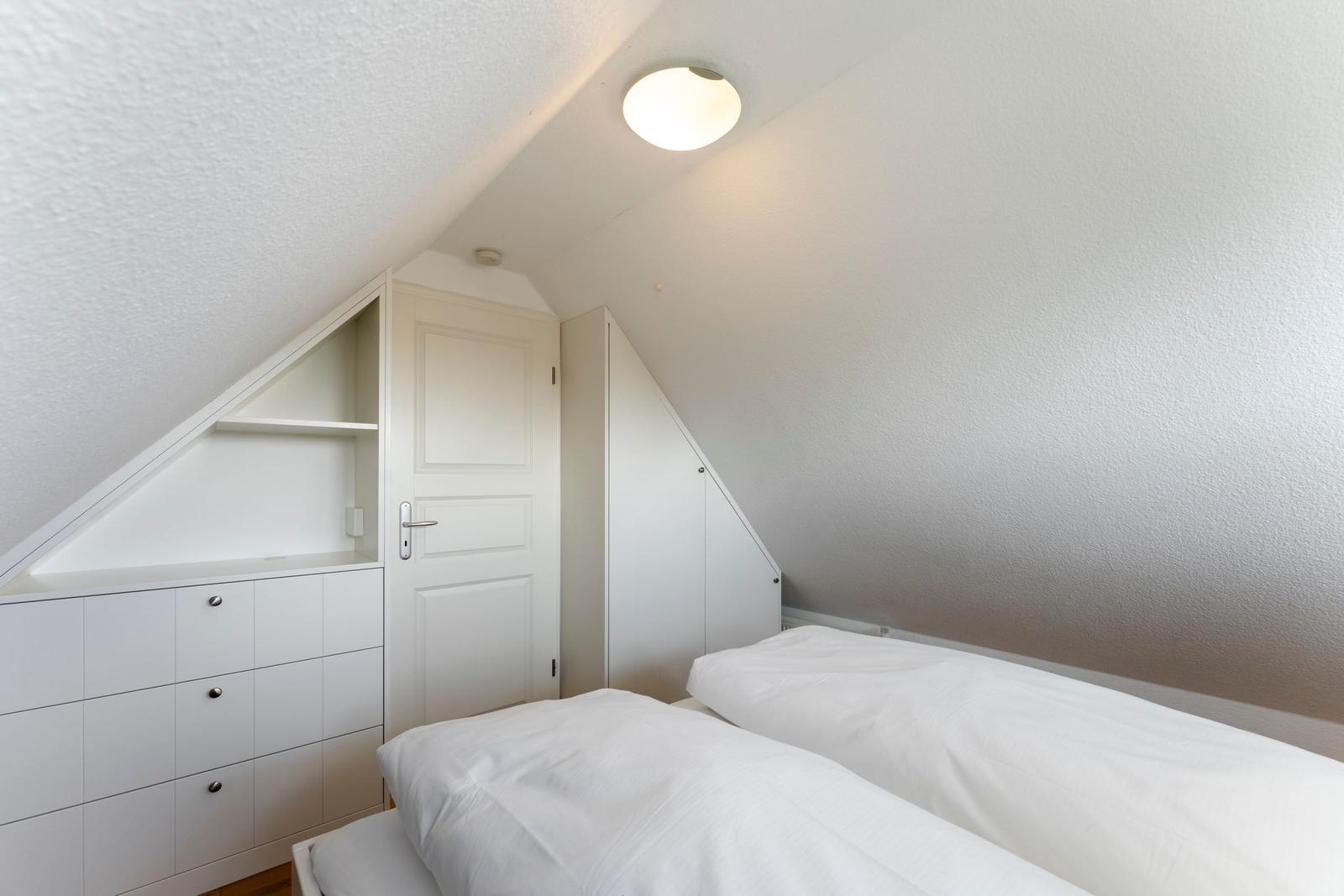 Zimmer mit Doppelbett, weißen Schränken und schrägen Wänden.