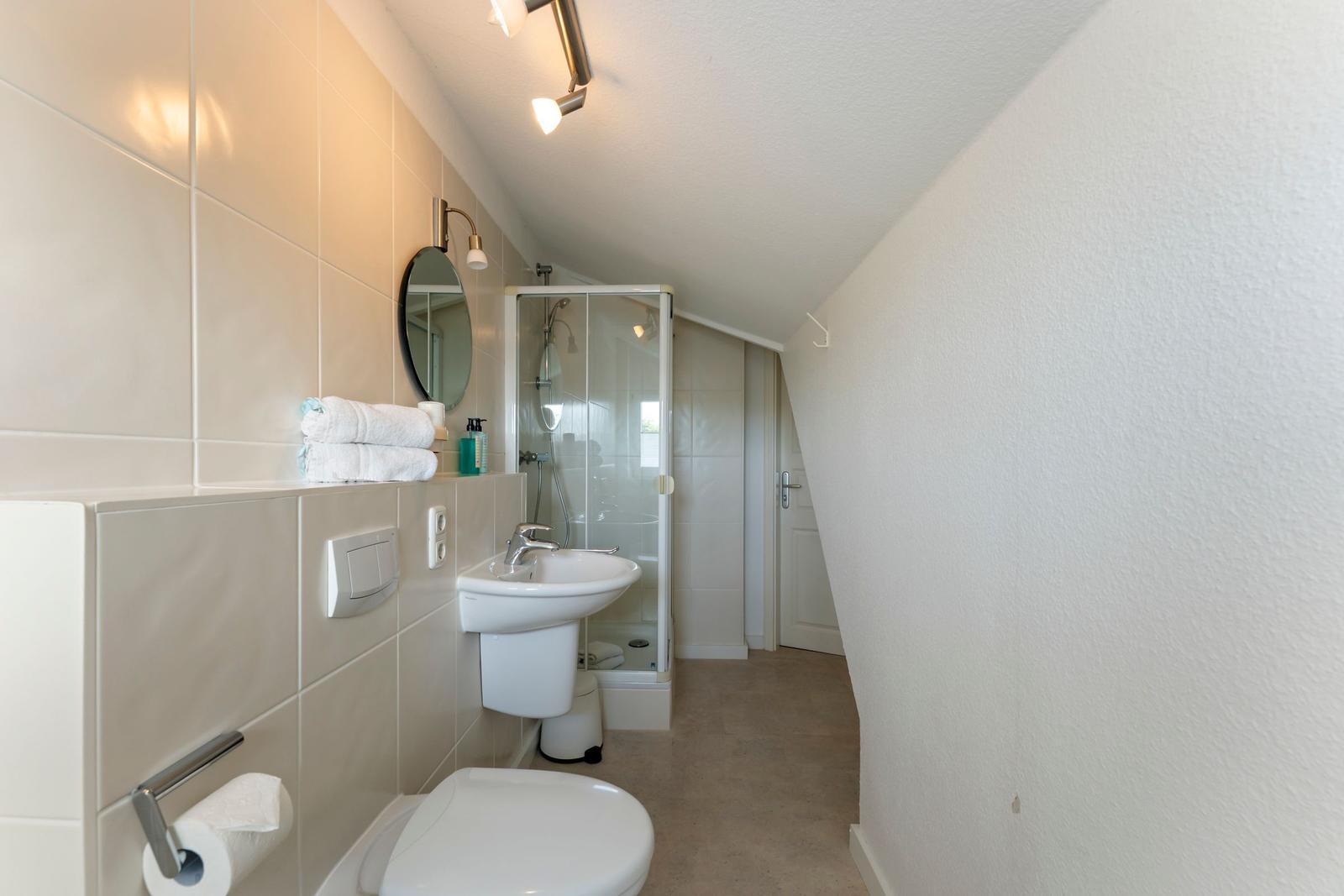 Badezimmer mit Dusche, Waschbecken und Toilette unter schrägem Dach