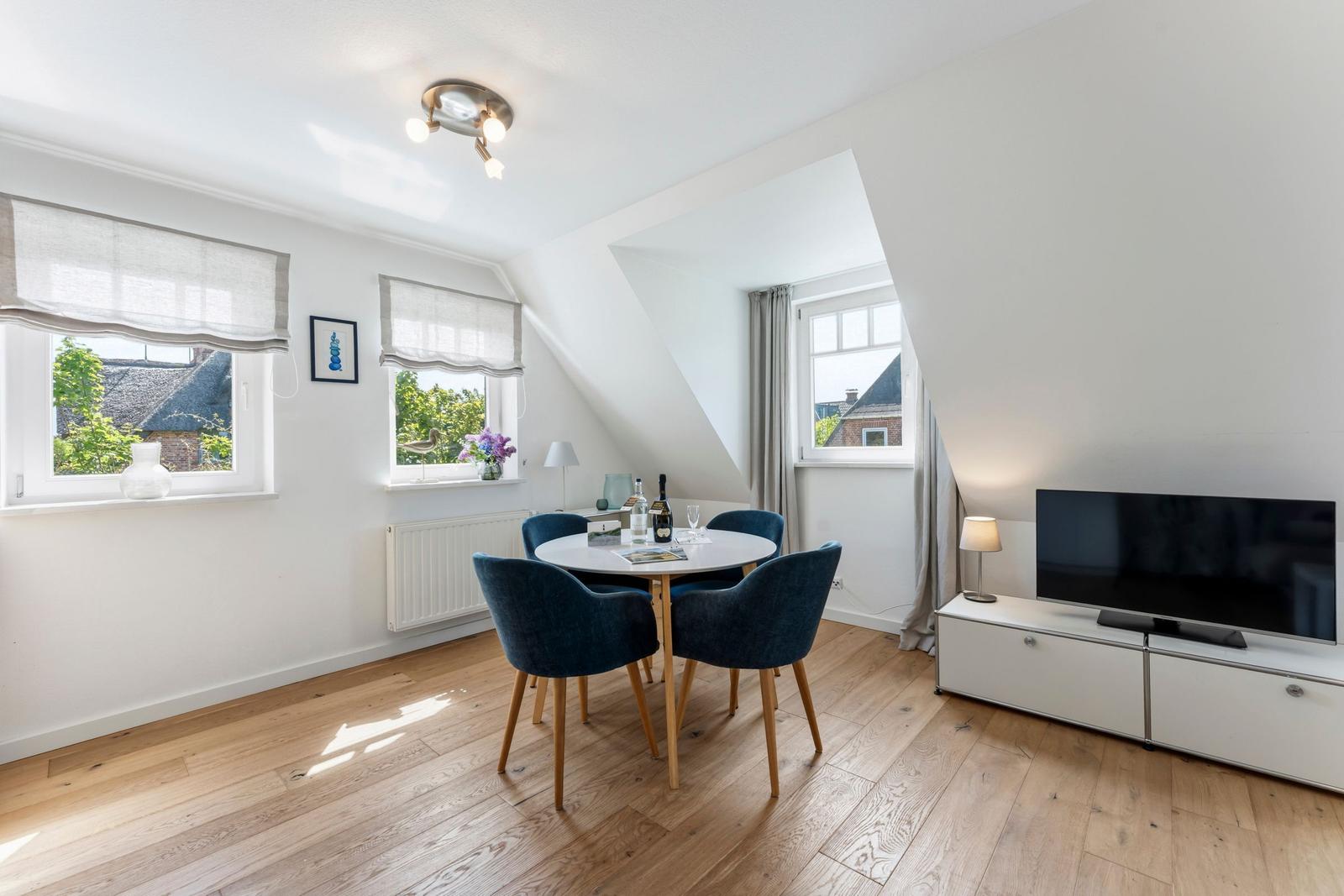 Dining room with round table, four chairs, TV, and windows.