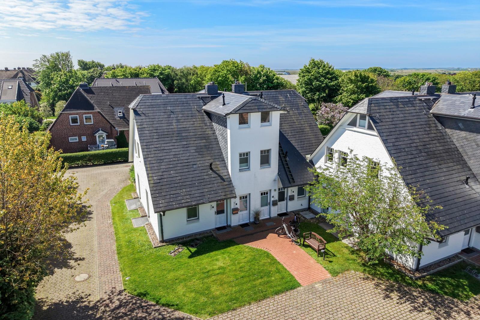 Haus mit weißer Fassade, schwarzem Dach und Gartenbereich mit Bank und Fahrrad.