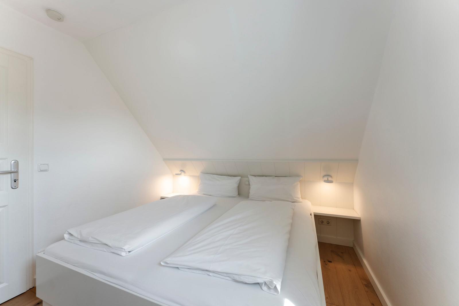 Schlafzimmer mit Doppelbett, weißen Laken und Holzboden. Dachschrägen an der Decke.
