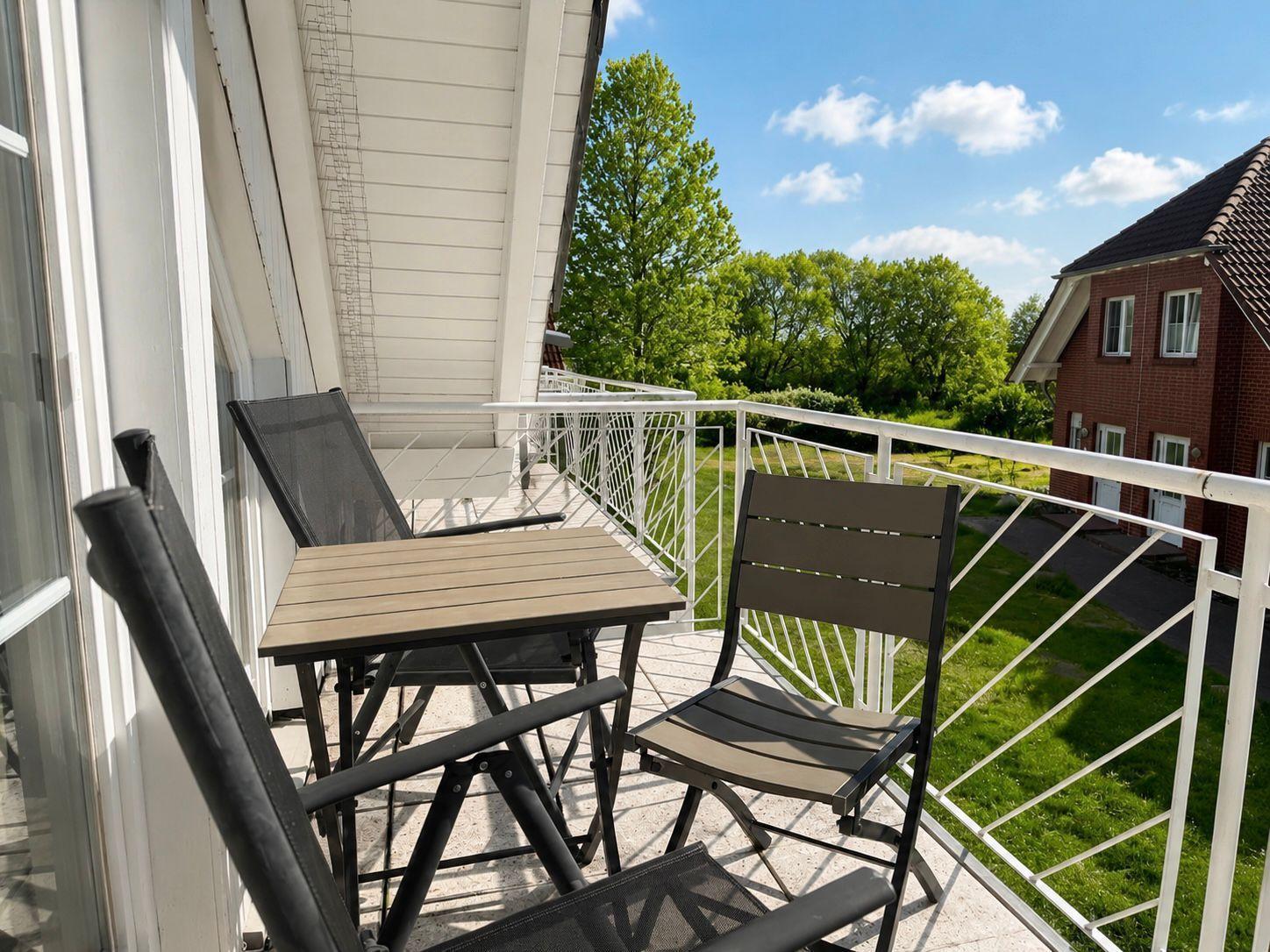 Balkon mit Tisch und Stühlen, Blick auf Grünfläche und Haus.