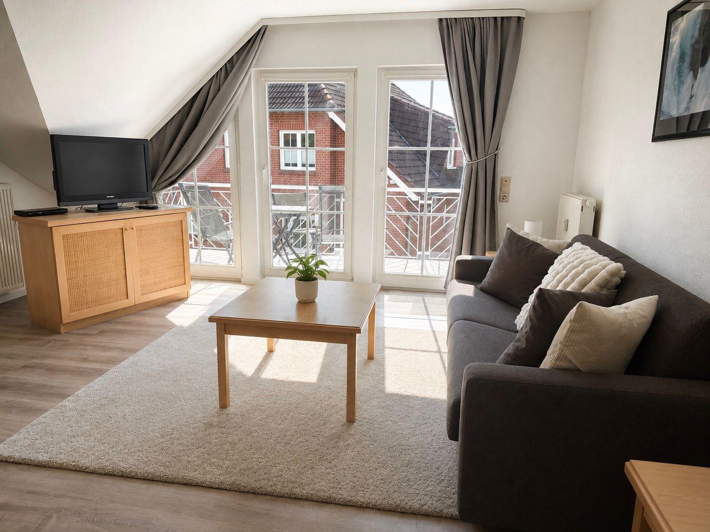 Wohnzimmer mit Sofa, Couchtisch und TV. Balkon mit Sitzgelegenheiten.