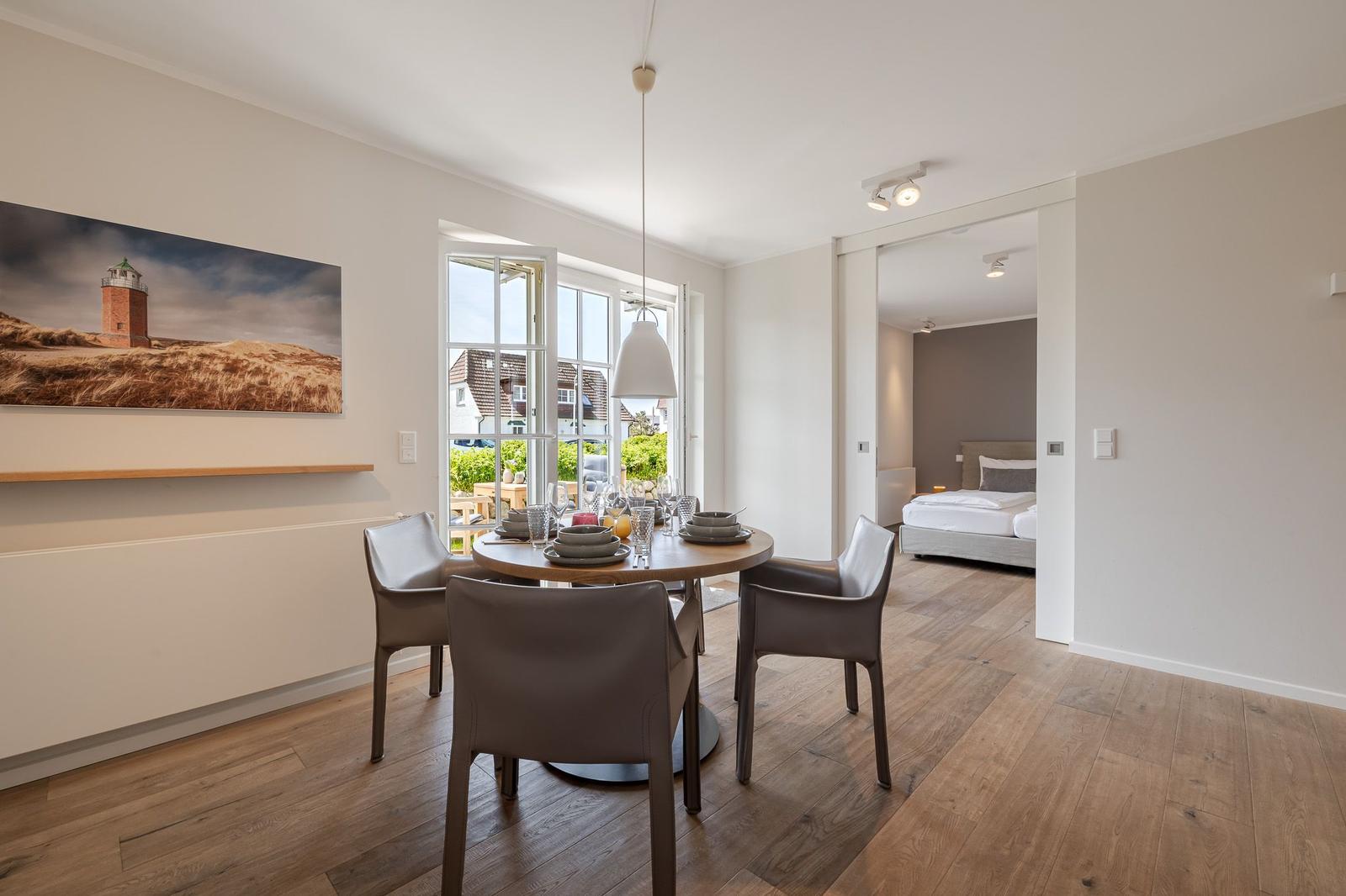Esszimmer mit Tisch, Stühlen und Blick auf Garten. Schlafzimmer ist im Hintergrund sichtbar.