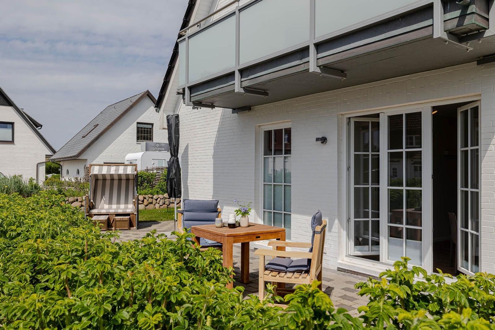 Terrasse mit Tisch, Stühlen und Liegestuhl. Hinterhof mit Pflanzen und Blick auf Haus.