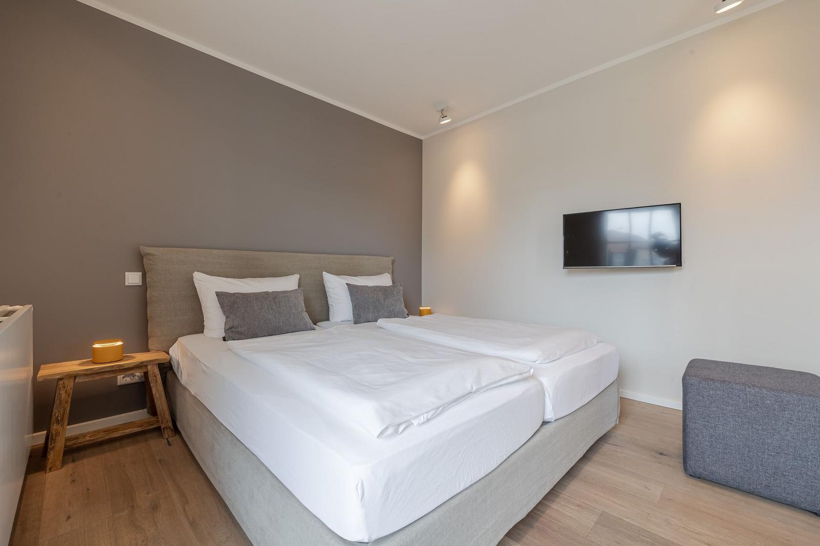 Schlafzimmer mit Doppelbett, Wand-TV und Holzboden.