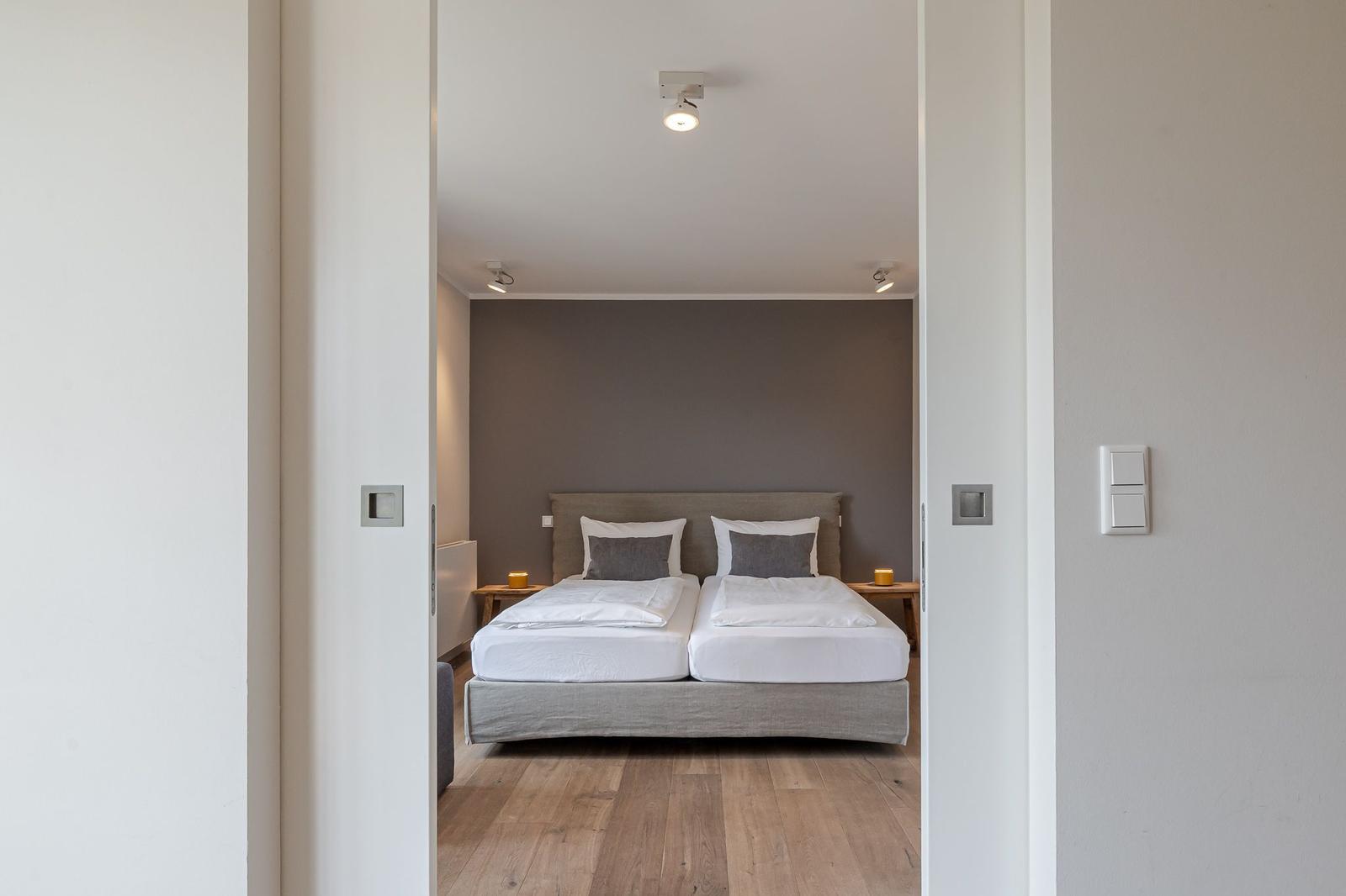 Schlafzimmer mit Doppelbett, Holzboden und grauer Wand.