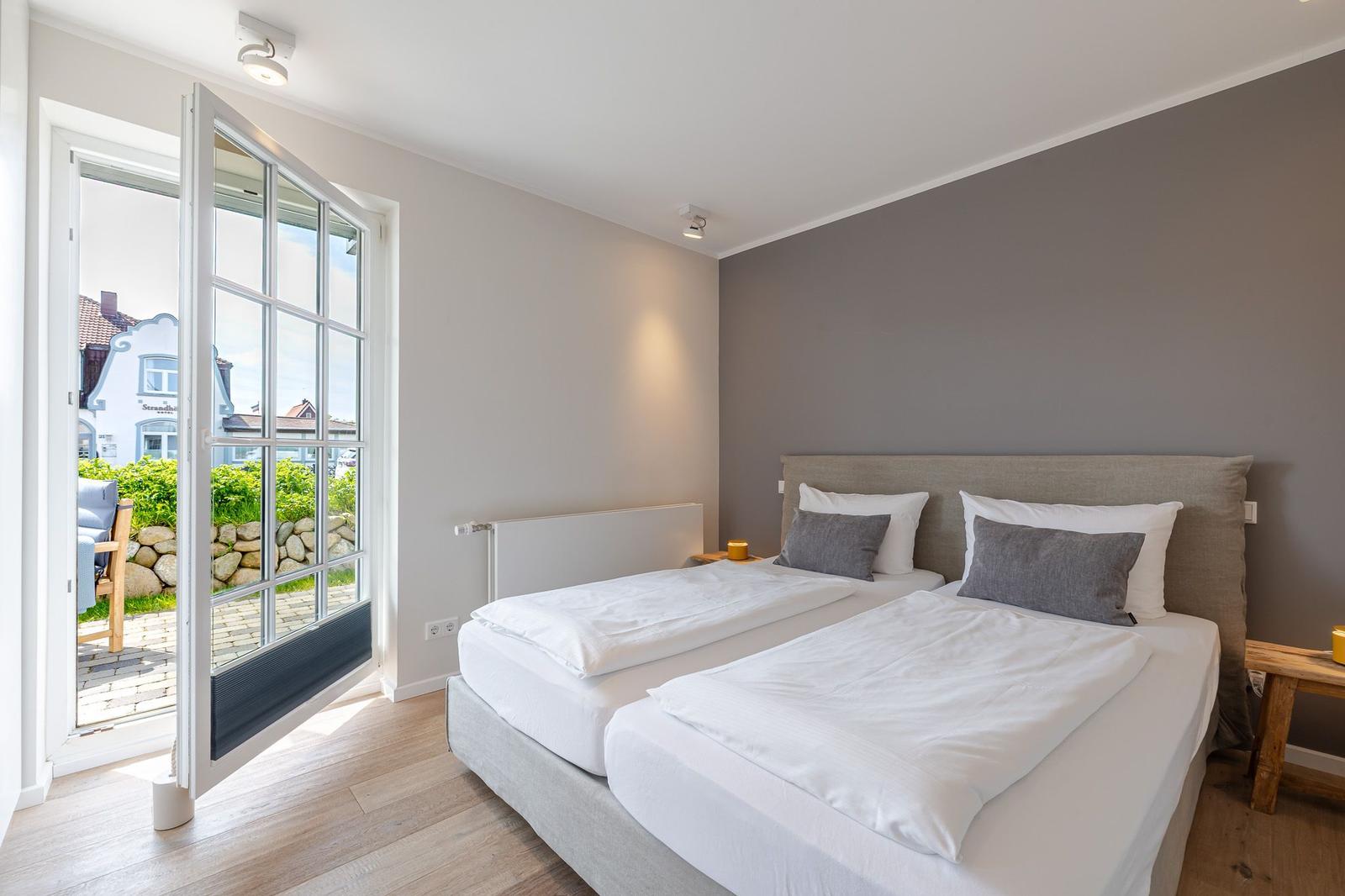 Doppelbett mit weißer Bettwäsche, Tür zum Balkon mit Gartenblick.