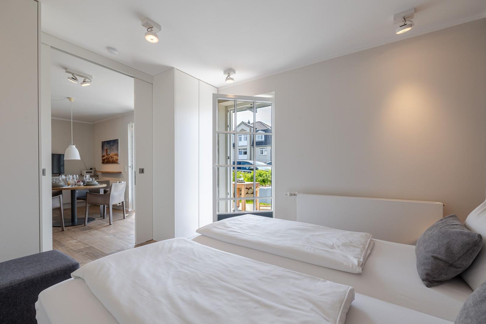 Schlafzimmer mit zwei Betten und Blick auf Balkon. Durchgang zur Küche sichtbar.