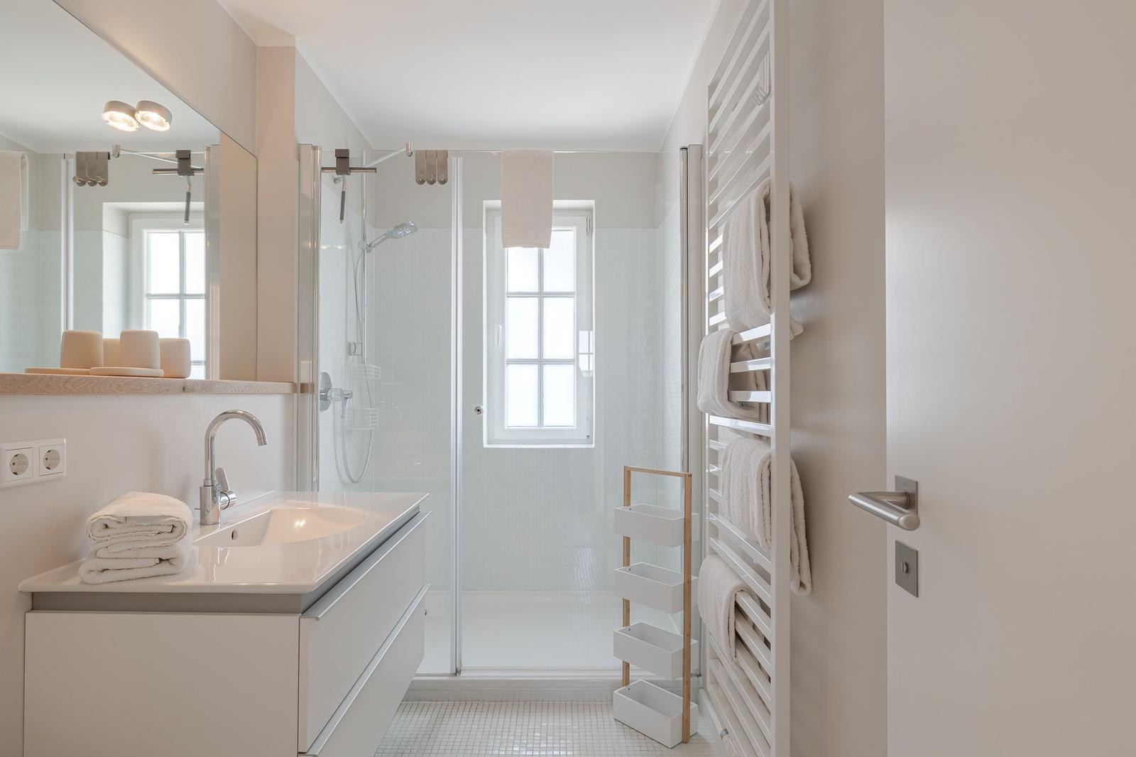 Badezimmer mit Dusche, Waschbecken und Heizkörper für Handtücher.