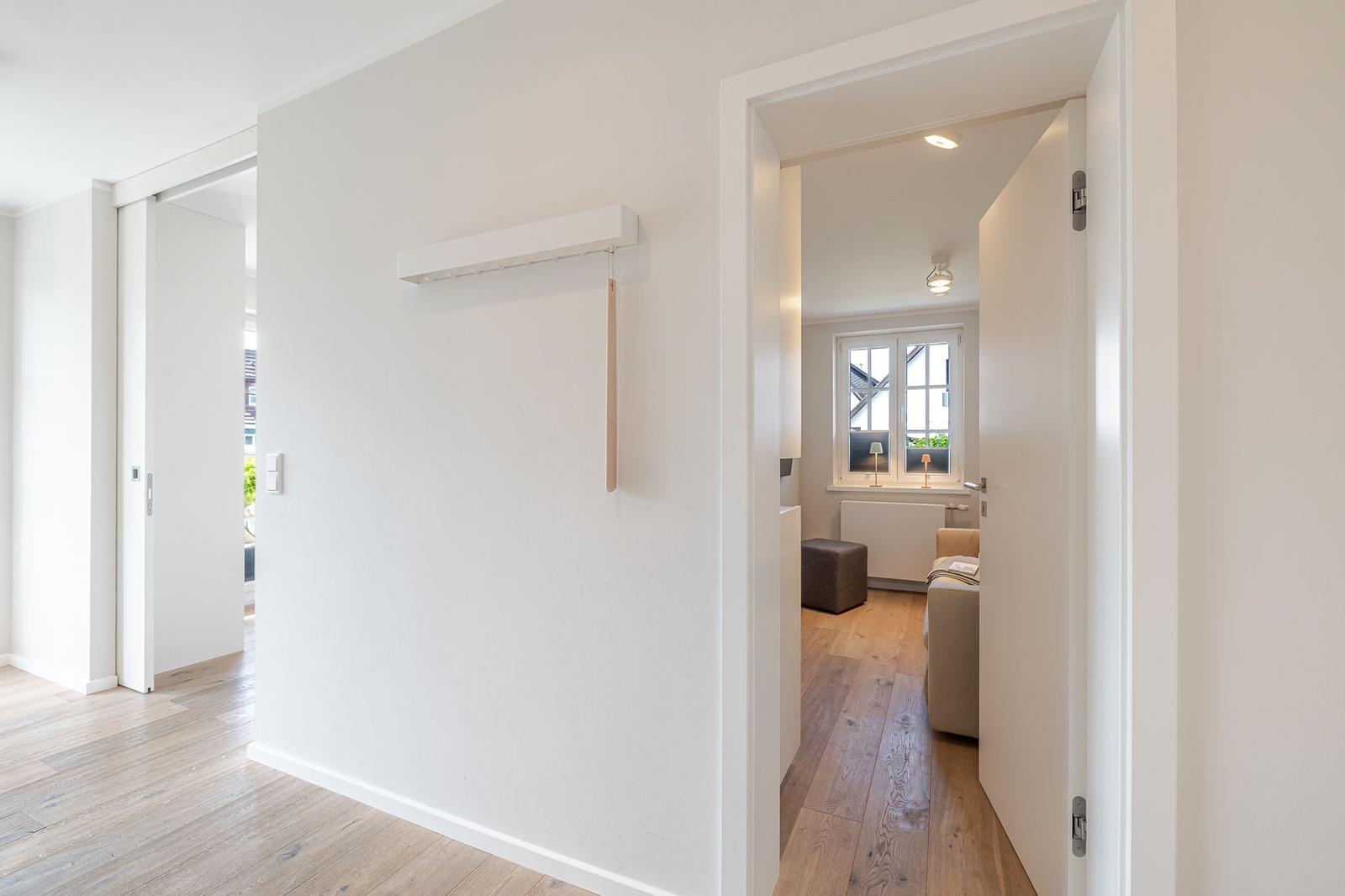 Hausflur mit Holzboden und Blick in Wohnzimmer mit Fenster und Sofa.