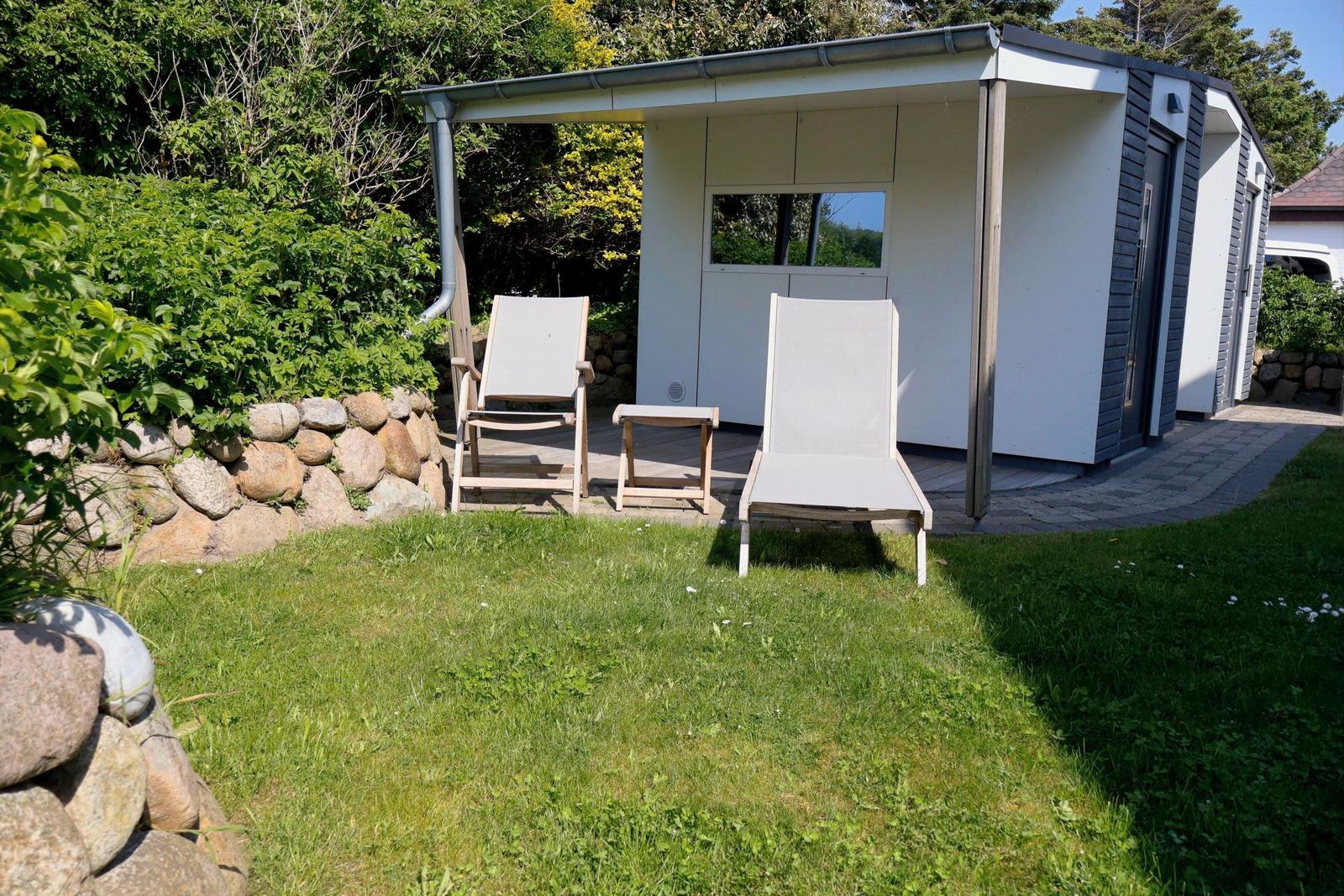 Zwei Liegestühle stehen vor einem modernen Gartenhaus mit Holzterrasse.