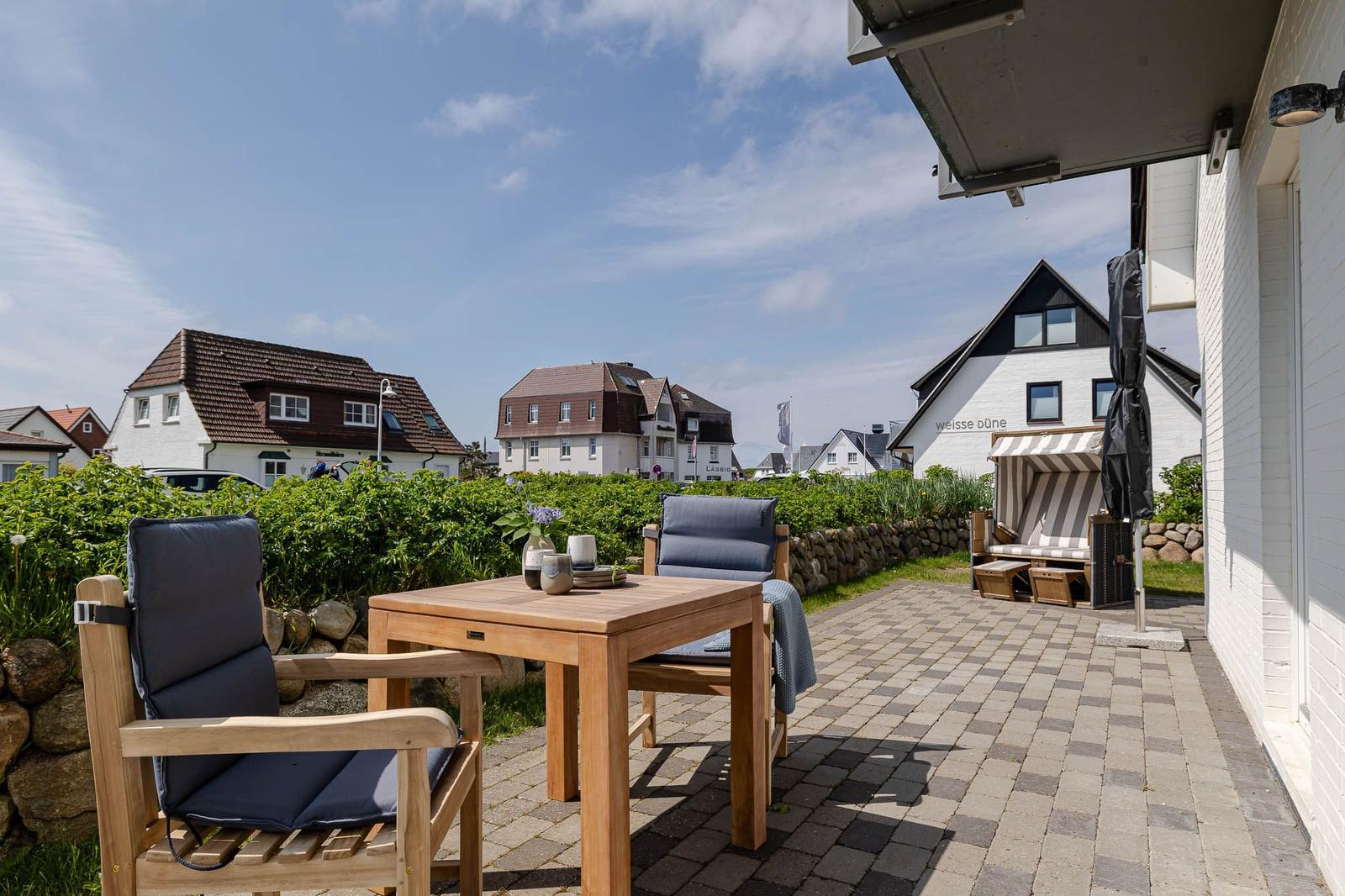 Terrasse mit Tisch und Stühlen, Blick auf Häuser und Strandkorb.