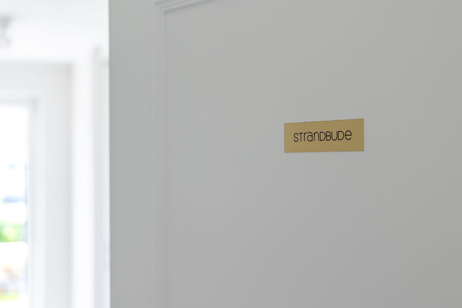 Schild mit der Aufschrift Strandbude an einer weißen Wand
