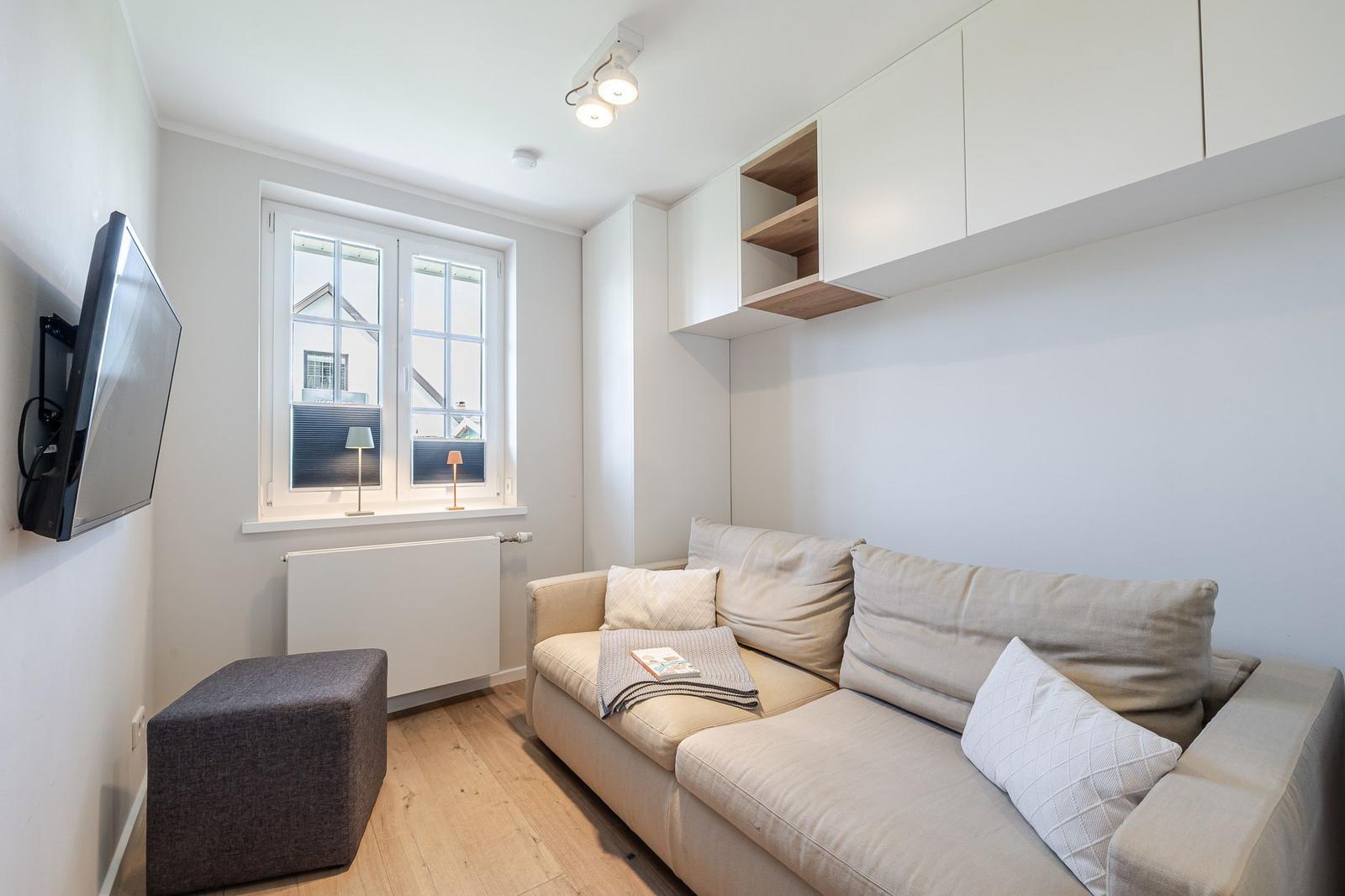 Wohnzimmer mit Sofa, Fenster, Fernseher und Schrank.