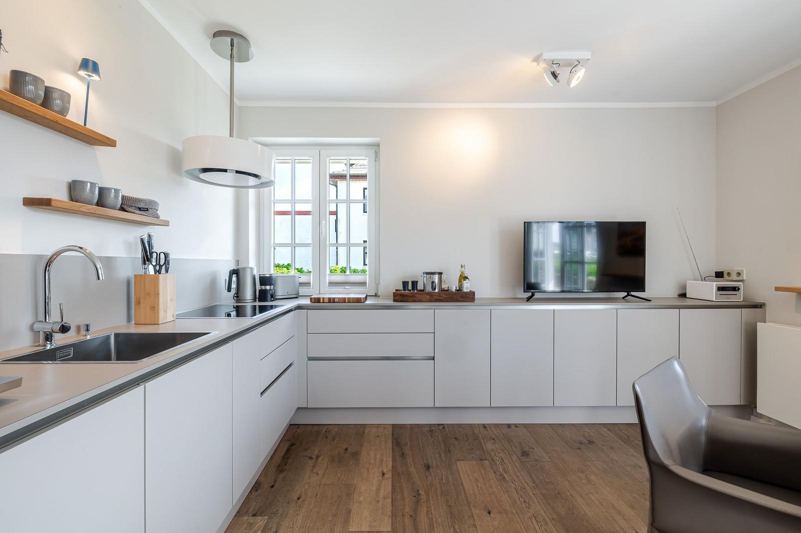 Moderne Küche mit weißen Schränken, Holzboden und Fenster mit Blick.