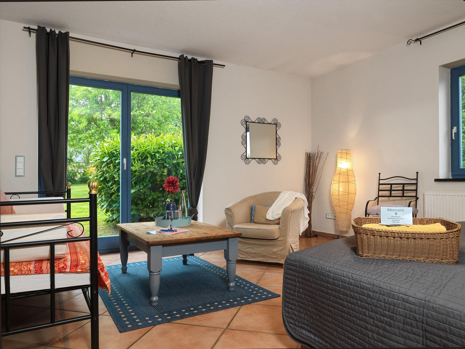 Zimmer mit Schlafbereich, Sitzgelegenheit und Blick auf den Garten.