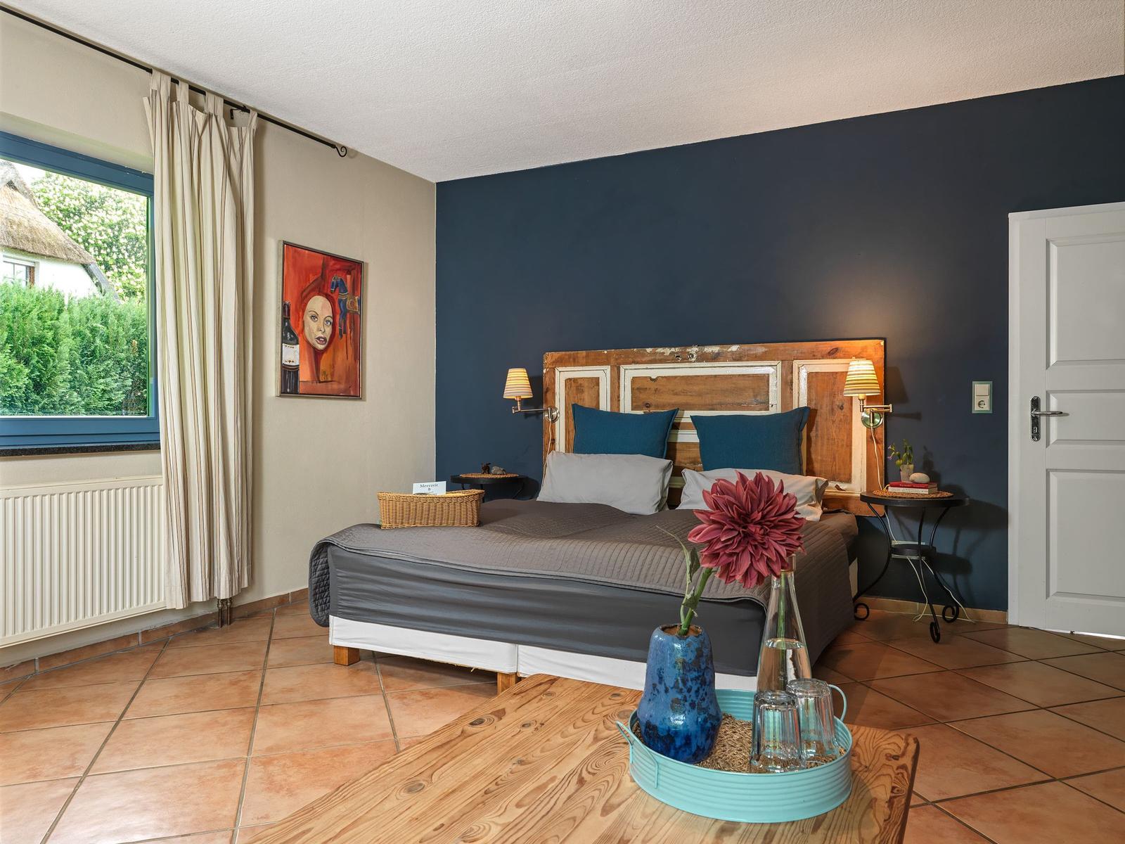Schlafzimmer mit Bett, Wandbild und Fenster mit Blick auf Garten.