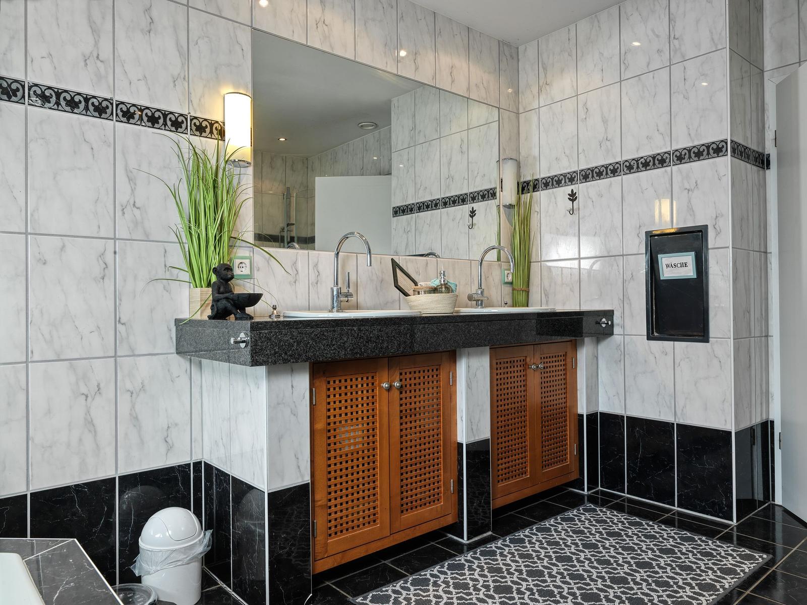 Badezimmer mit Marmorwand, Waschbecken und Holzschränken.