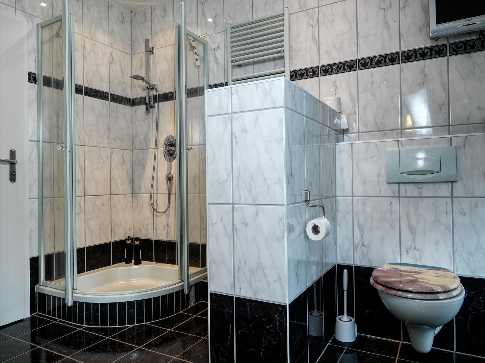 Bad mit Dusche, Toilette und Heizung. Marmor- und Fliesenverkleidung.