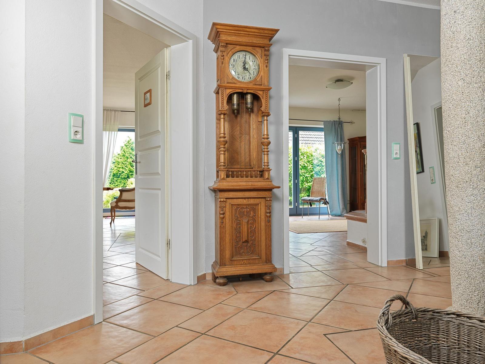 Hausflur mit antikem Holzuhrenschrank, Fliesenboden und Blick in angrenzende Räume.