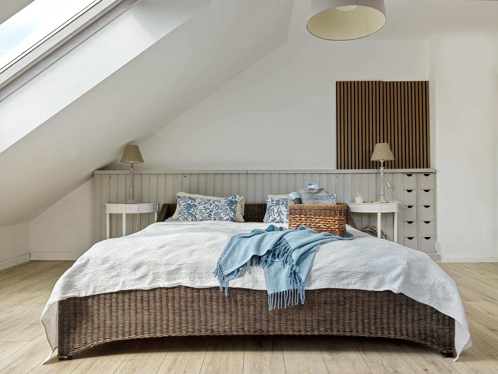 Schlafzimmer mit Dachschrägen, Wickerbett, zwei Nachttischen und Holzboden.