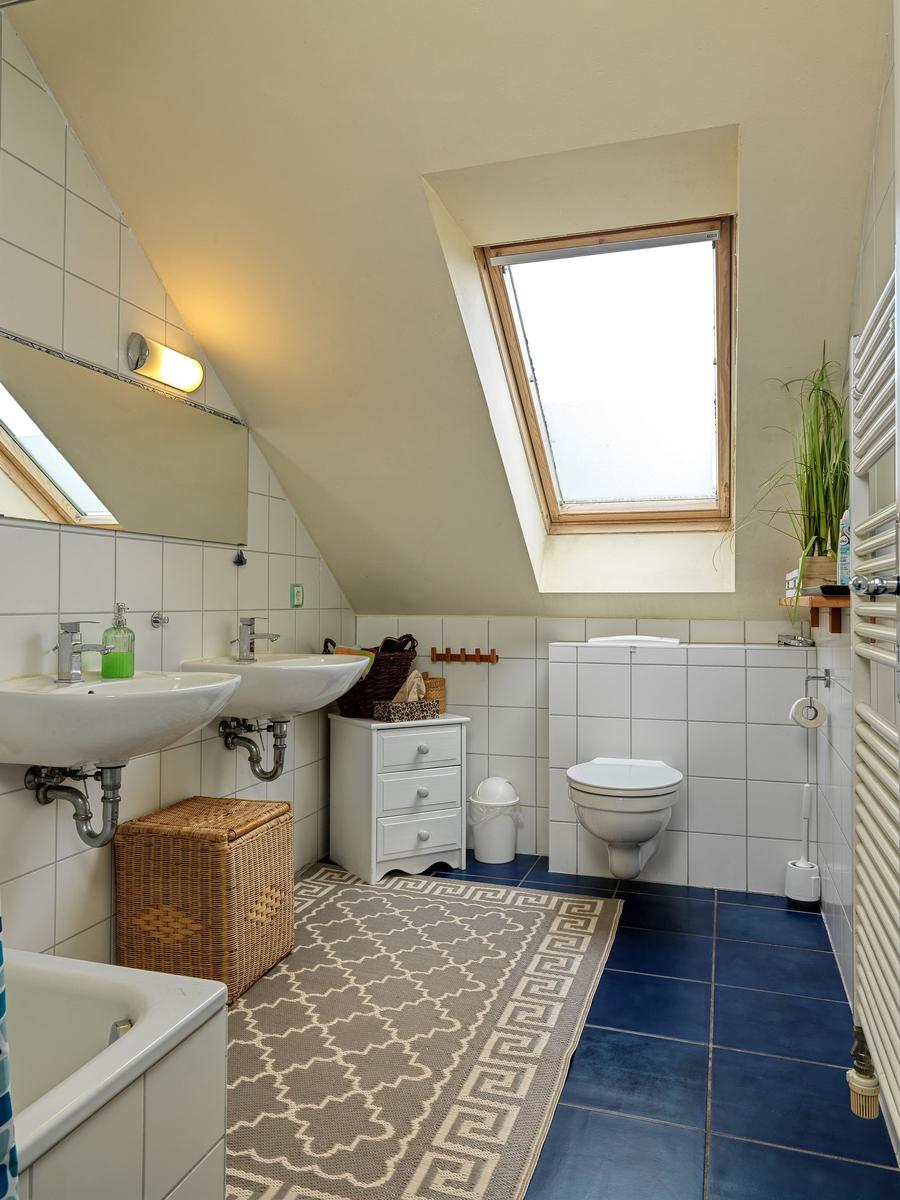 Badezimmer mit Dachschrägen, Dusche, Toilette und Waschbecken.