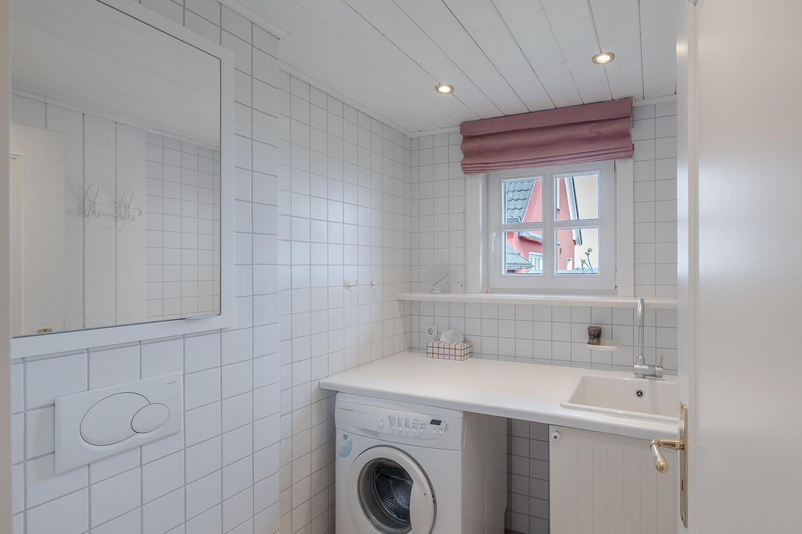 Waschraum mit Waschmaschine, Spüle und Fenster mit rotem Rollladen.