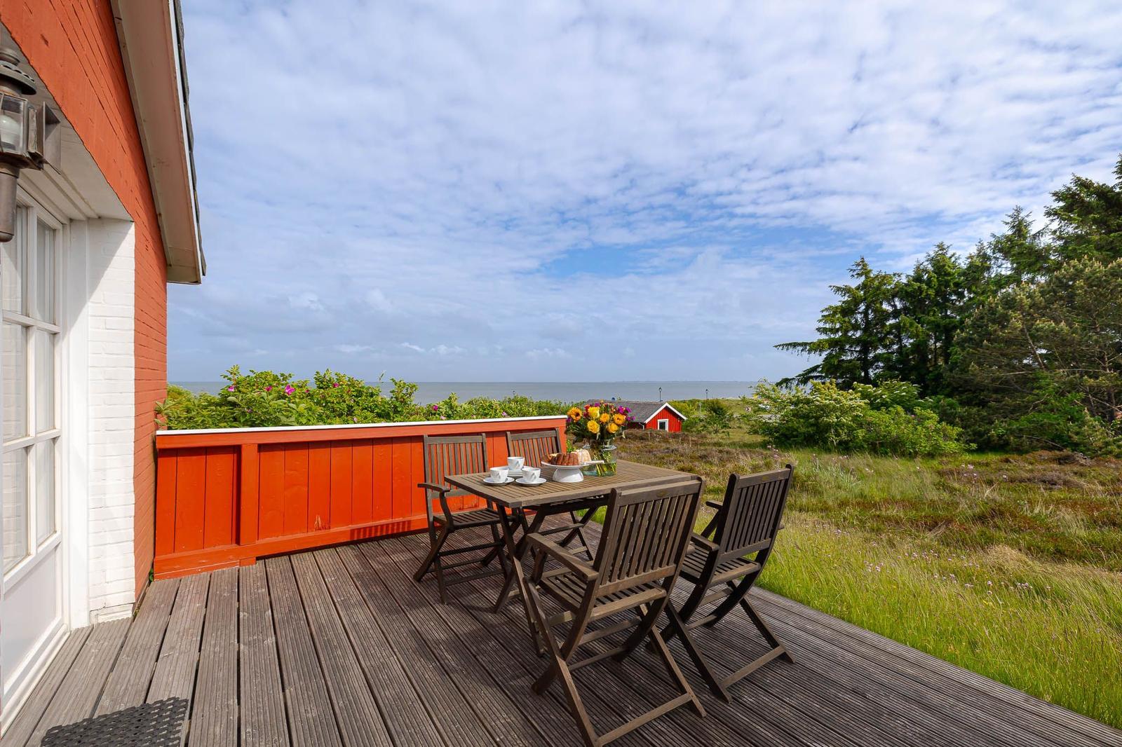Terrasse mit Tisch und Stühlen, Blick auf Meer und grüne Landschaft.