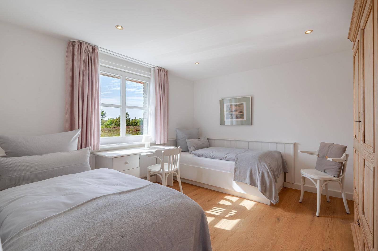 Zimmer mit zwei Betten, Schreibtisch und Fenster mit Blick auf Grünfläche.