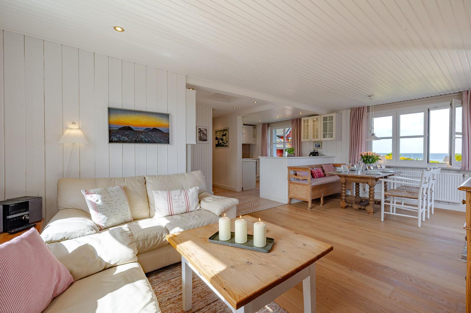 Wohn- und Essbereich mit Holzboden, Sofa, Tisch und Küchenbereich mit Meerblick.