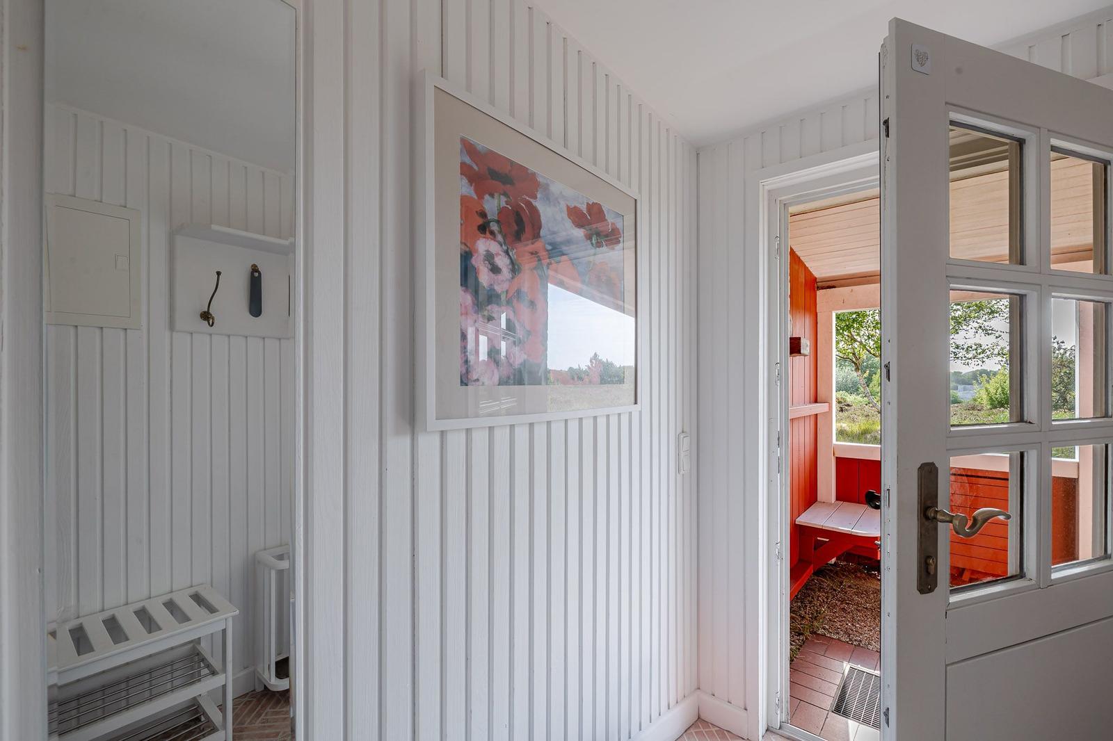 Haus mit weiß verkleideten Wänden, Bild an der Wand und Tür zum Außenbereich.