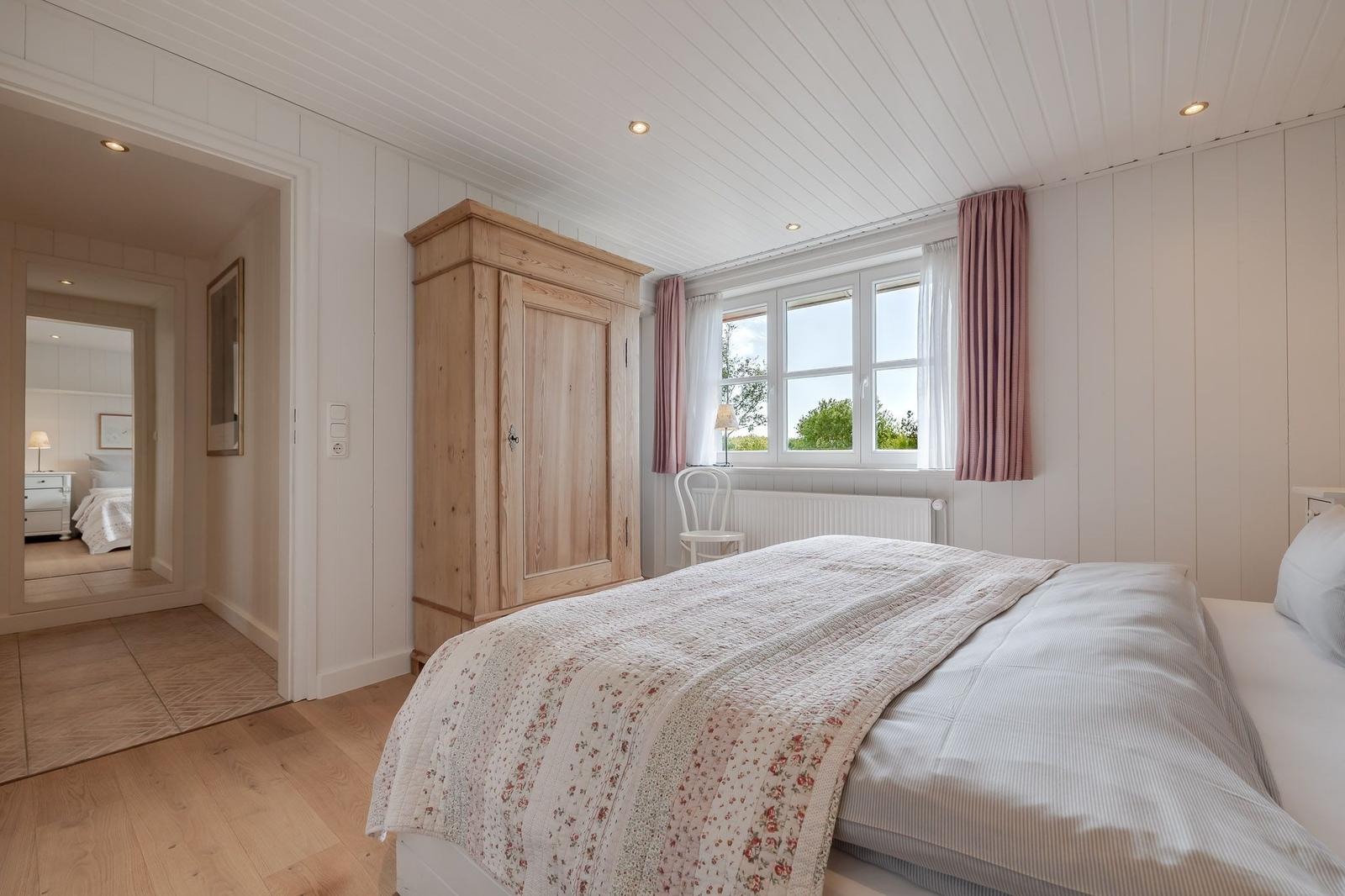 Schlafzimmer mit Bett, Holzschrank und Fenster mit Blick auf Grün.