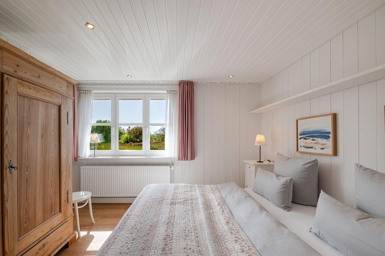 Schlafzimmer mit Bett, Kleiderschrank und Fenster zum Garten.
