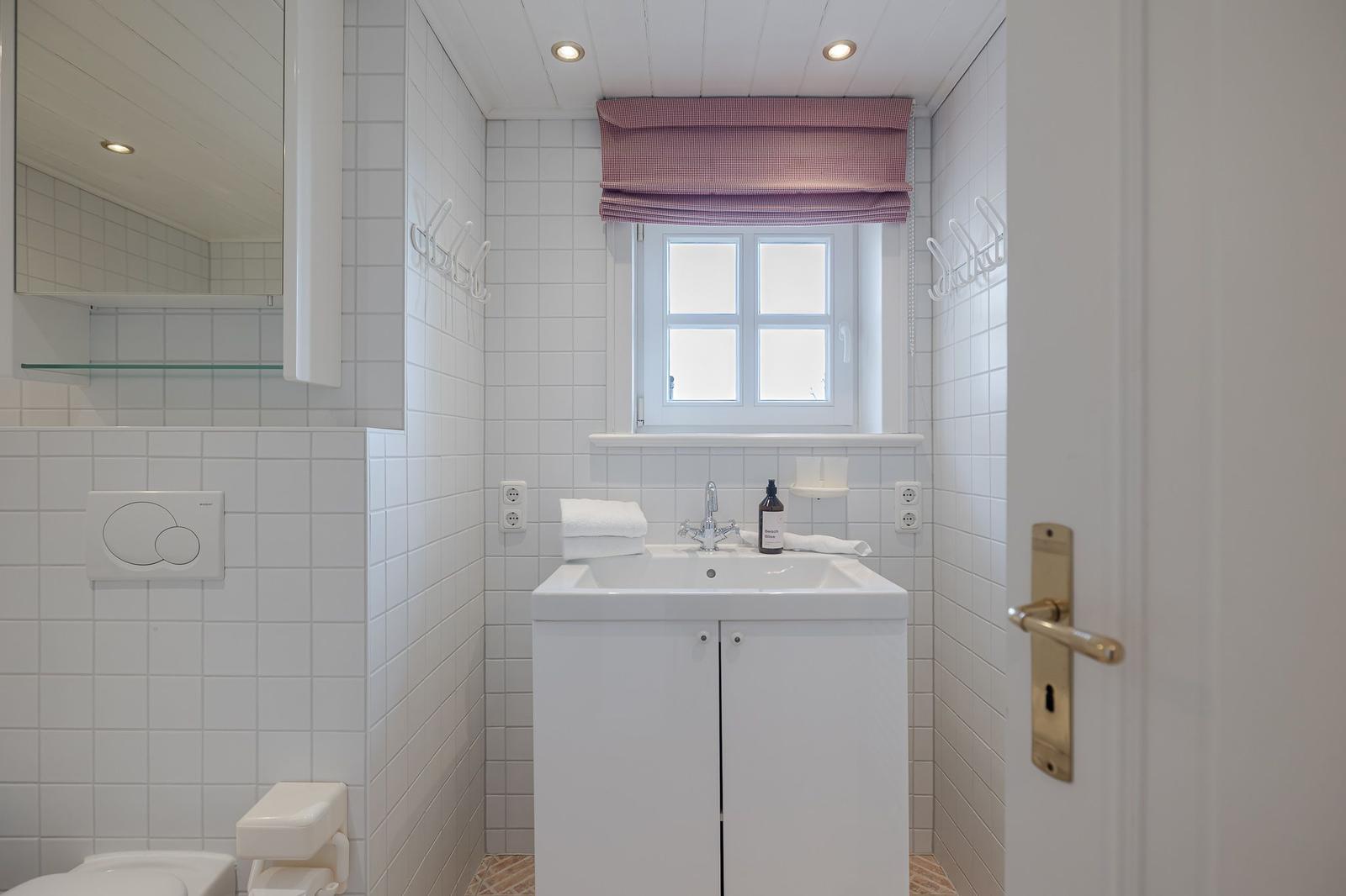 Badezimmer mit Waschbecken, Toilette und Fenster mit Rollladen.