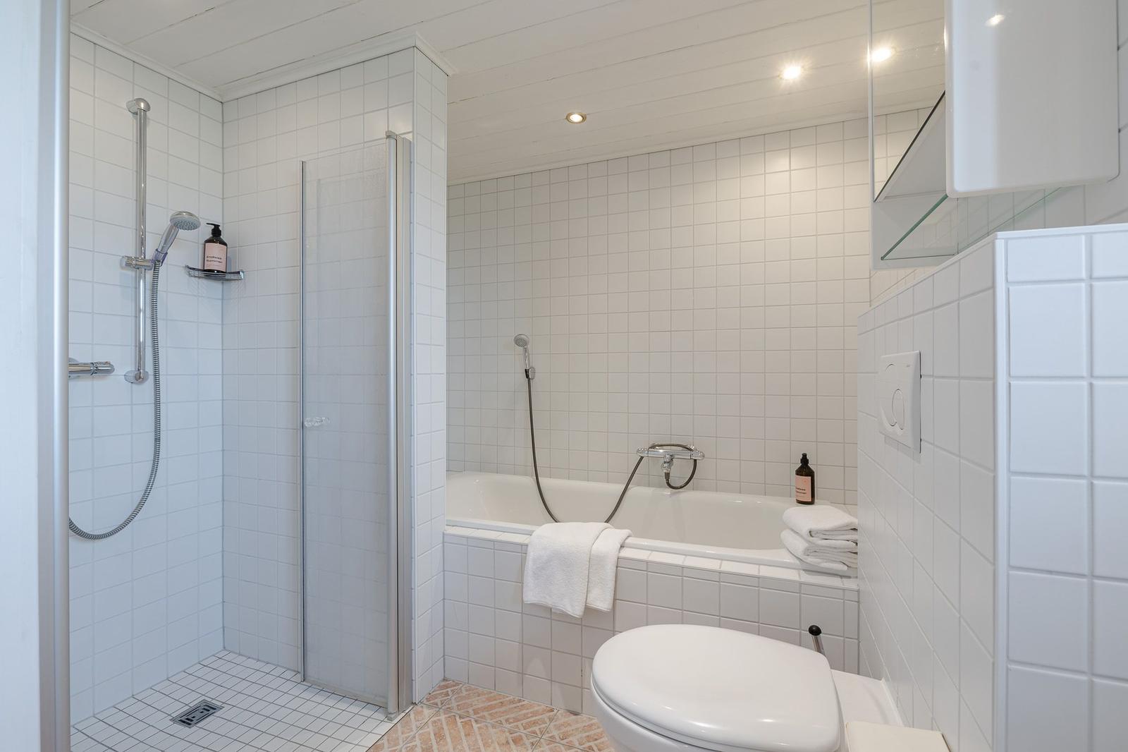 Badezimmer mit Dusche, Badewanne und Toilette. Weiße Fliesen und moderne Einrichtung.
