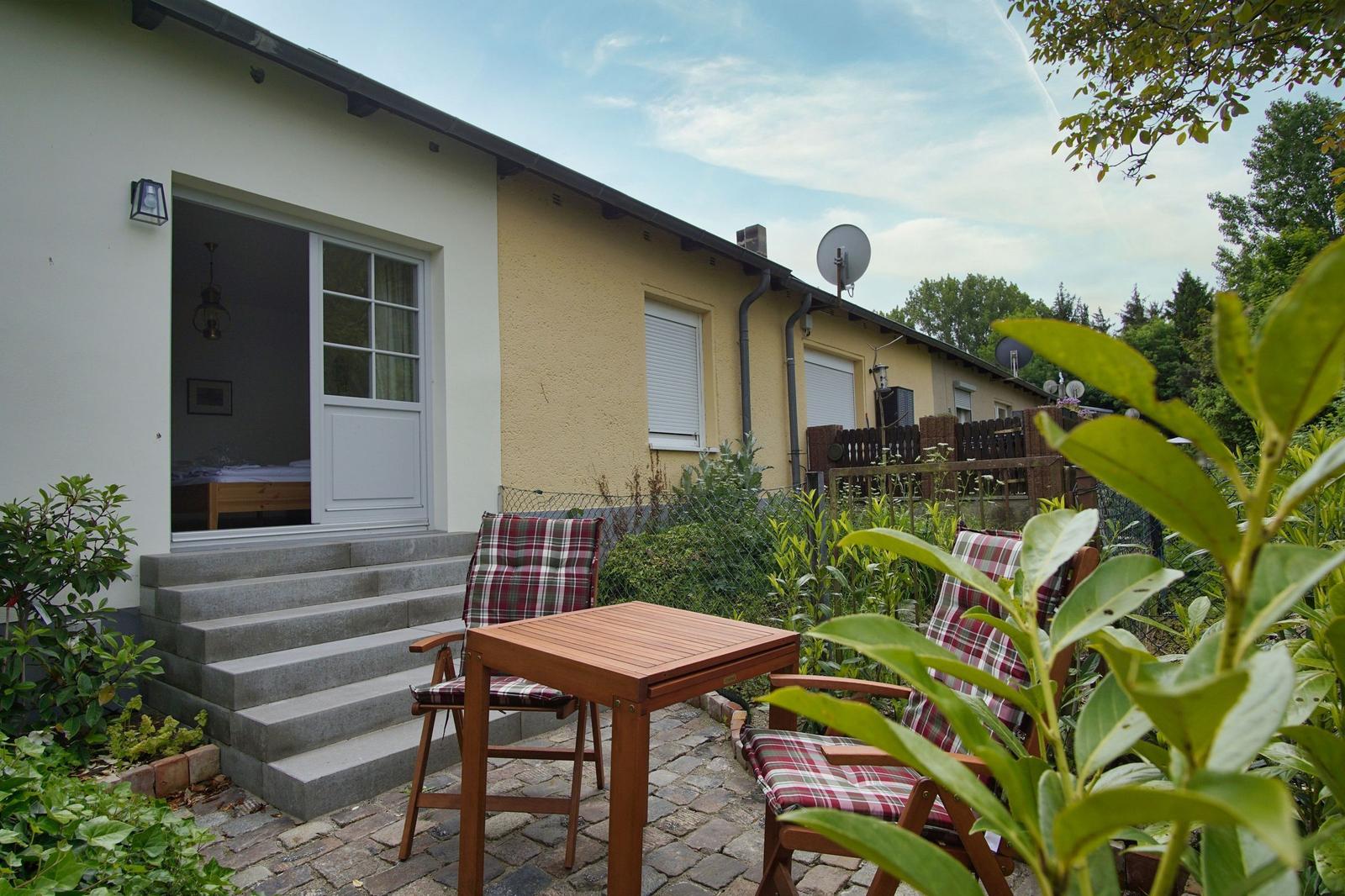 Haus mit Terrasse, Tisch und Stühlen. Durchgangstür führt ins Schlafzimmer.