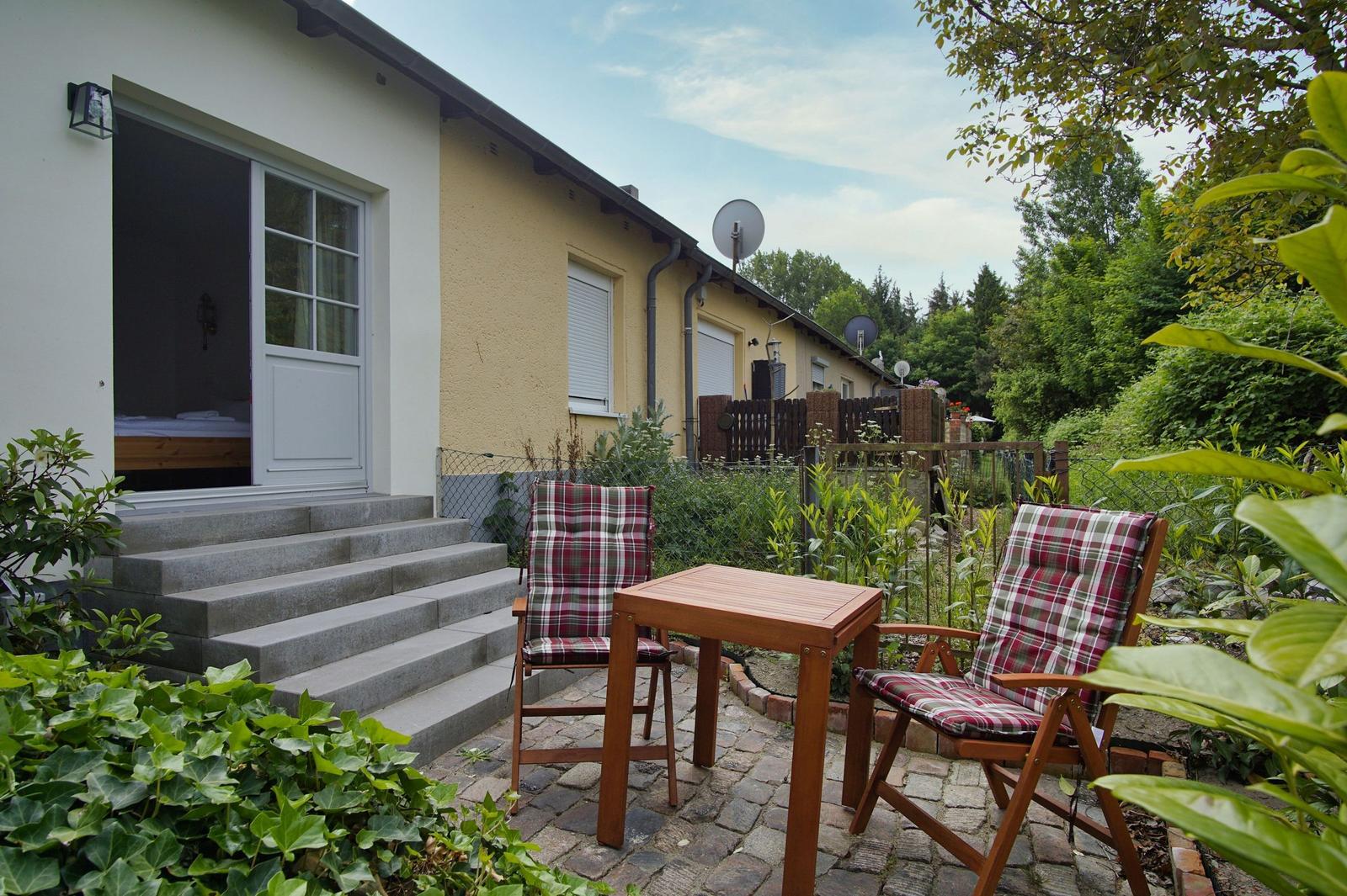 Terrasse mit Tisch und zwei Stühlen vor einem Haus mit Garten.