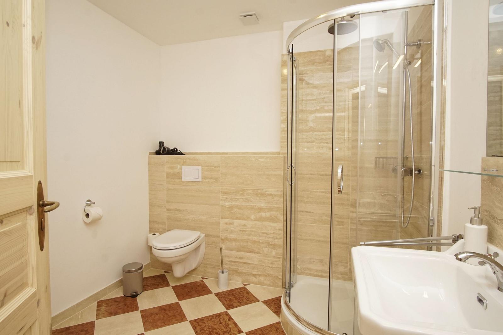 Badezimmer mit Dusche, Waschbecken und Toilette. Fliesenboden und Wandverkleidung.