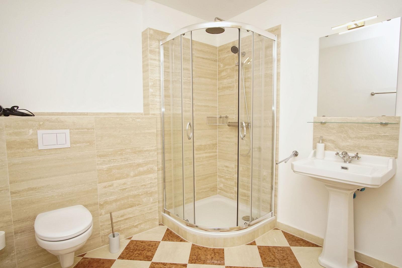 Badezimmer mit Dusche, Waschbecken und Toilette. Fliesen und Spiegel sichtbar.