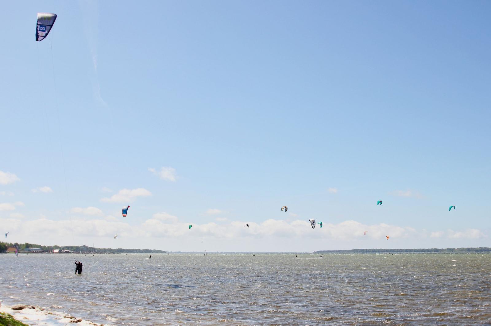 Kitesurfen auf dem Wasser unter blauem Himmel mit mehreren bunten Kites.