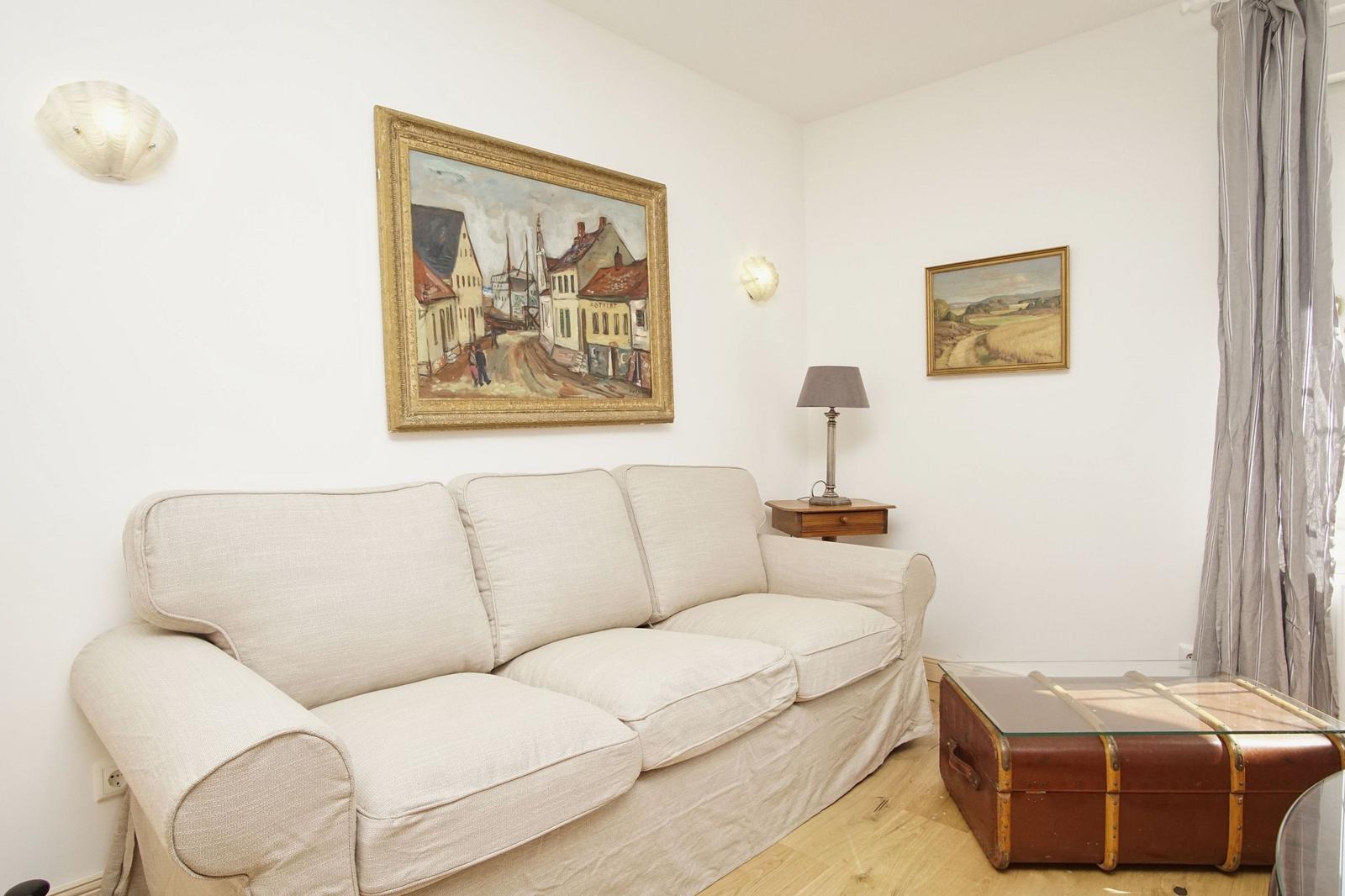 Ein Wohnzimmer mit einem cremefarbenen Sofa, zwei Bildern an der Wand und einem Holzboden.