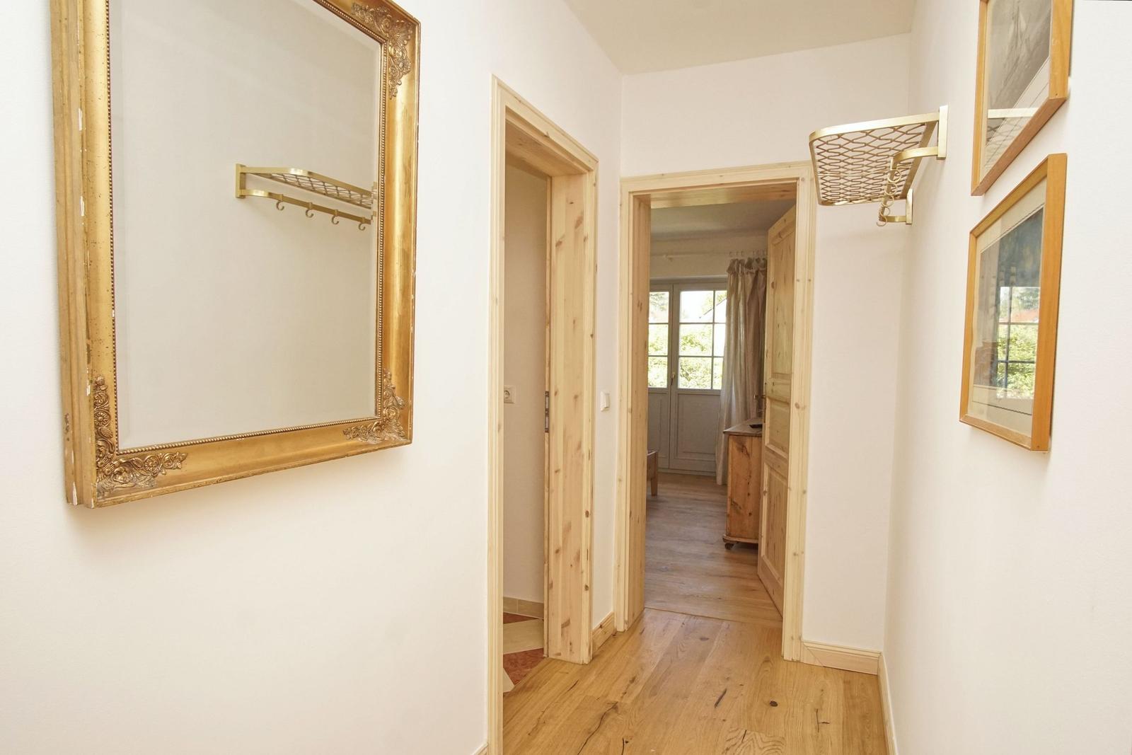 Flur mit Holzboden, goldgerahmtem Spiegel und Bildern an der Wand.