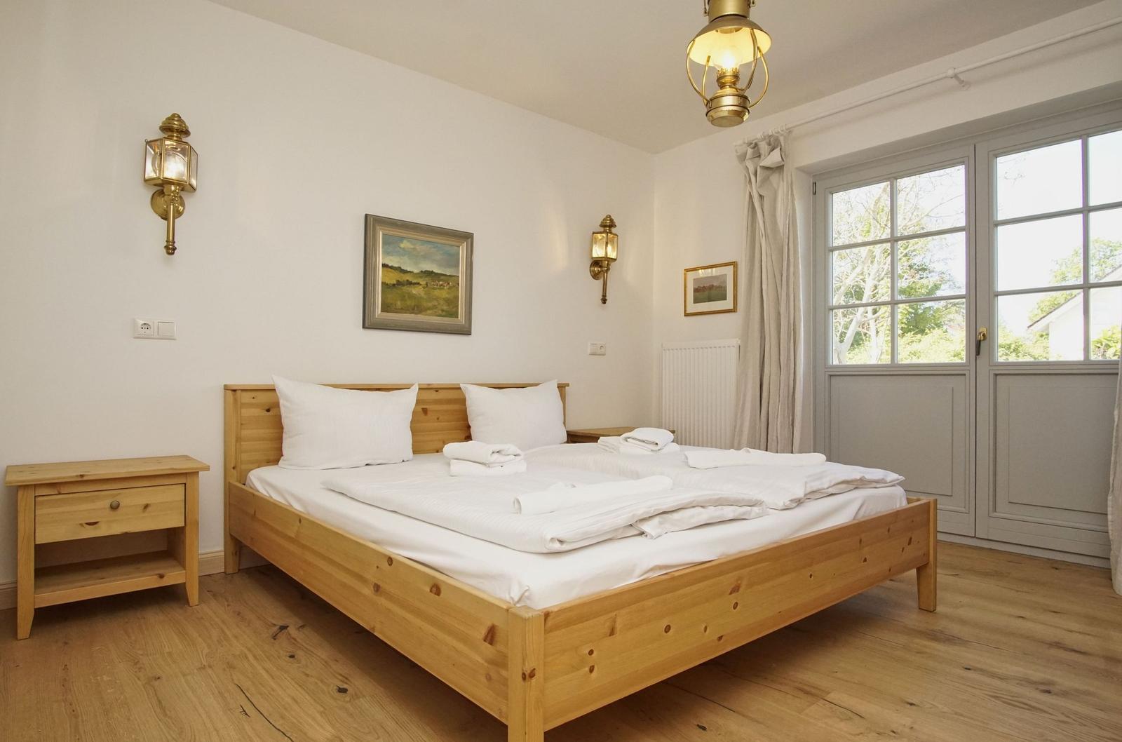 Schlafzimmer mit Holzbett, Nachttisch und Fenster. Deckenleuchte und Wandlampen.