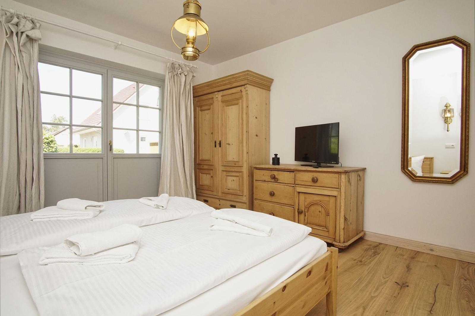 Schlafzimmer mit Holzbett, Schrank und Fernseher. Fenster mit Blick auf Garten.
